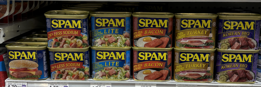 A grocery store shelf neatly stocked with two rows of various flavors of SPAM canned meat.